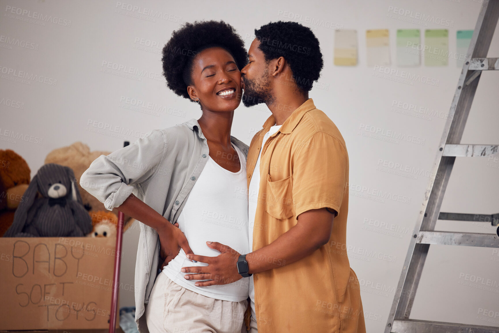 Buy stock photo Love, pregnancy or black couple kiss in home renovation, diy or house remodel together by apartment ladder. Hugging, happy smile or African man and pregnant woman excited about baby or new family 