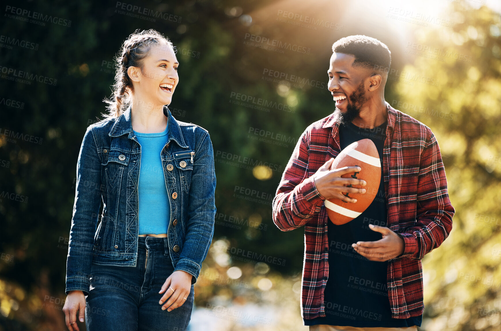 Buy stock photo Couple laughing, American football in park and happy together in nature, walking outdoor and sports in the sun. Commitment, trust and fitness, black man and woman, interracial couple and funny joke