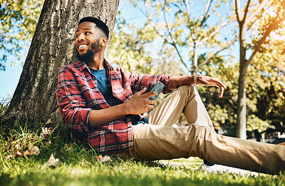 Buy stock photo Nature, phone and man sitting by a tree in an outdoor park networking on social media or the internet. Technology, rest and African guy browsing on mobile app with cellphone while relaxing in garden.