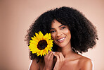 Black woman, studio portrait and sunflower with smile, beauty and cosmetic wellness by beige background. African gen z model, flower and spring aesthetic with happiness, makeup and natural makeup