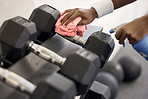 Dumbbells, cleaner and hands cleaning at a gym with liquid soap in spray bottle with cloth for wellness. Janitor or person wipes dirty bacteria on dusty weights, tools or fitness training equipment 