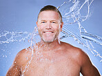 Portrait, water splash and mature man in studio for cleaning, hygiene and wellness on a blue background. Skincare, face and body care for aging skin of male model in luxury, pamper or beauty routine