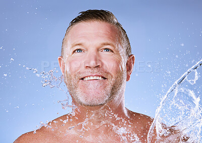 Buy stock photo Wellness, water splash and senior man cleaning, morning routine and washing on blue studio background. Male, mature gentleman and daily hygiene with clear liquid for dermatology, skincare or grooming