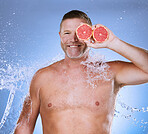 Grapefruit in hand, water splash and man with face, beauty and skincare, eco friendly and organic on blue background. Hydration, vitamin c and hygiene, senior male in portrait, smile and citrus fruit