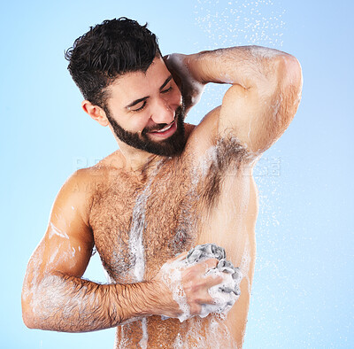 Buy stock photo Shower, cleaning and man with sponge, soap and water splash in studio for wellness, hygiene and grooming. Skincare, health and happy male with foam, cosmetics and washing body on blue background 