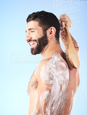 Buy stock photo Shower, brush and man cleaning body with soap, foam and water splash for wellness, hygiene and grooming. Skincare, self care and happy male with smile, bath cosmetics and washing on blue background