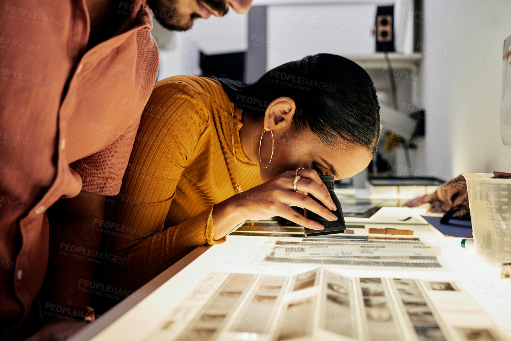 Buy stock photo Photography, editing and film negatives for looking, magnifying glass or zoom analysis at photo journalist job. Photographer man, analyse or focus with woman in studio for creative choice in teamwork