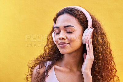 Buy stock photo Music, quiet and peaceful with a black woman listening to the radio outdoor on a yellow wall background. Headphones, energy and face with an attractive young female streaming audio sound for fun