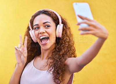 Buy stock photo Black woman, peace selfie and music headphones on yellow wall background for freedom. Happy and excited gen z person outdoor listening to podcast audio with hand sign or emoji for influencer post