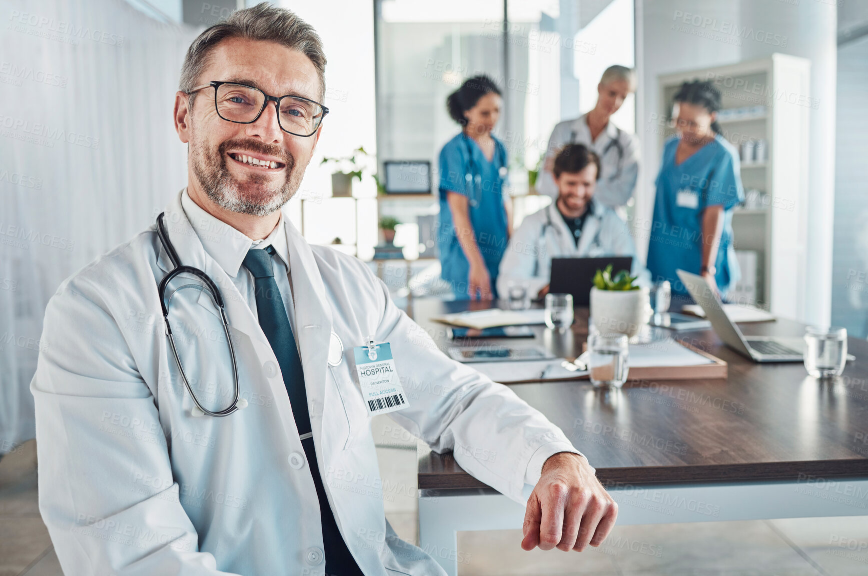 Buy stock photo Healthcare, smile and portrait of senior doctor at desk in teaching hospital office with nurses and medical students. Health, medicine and leadership with mature mentor and smiling man at clinic.