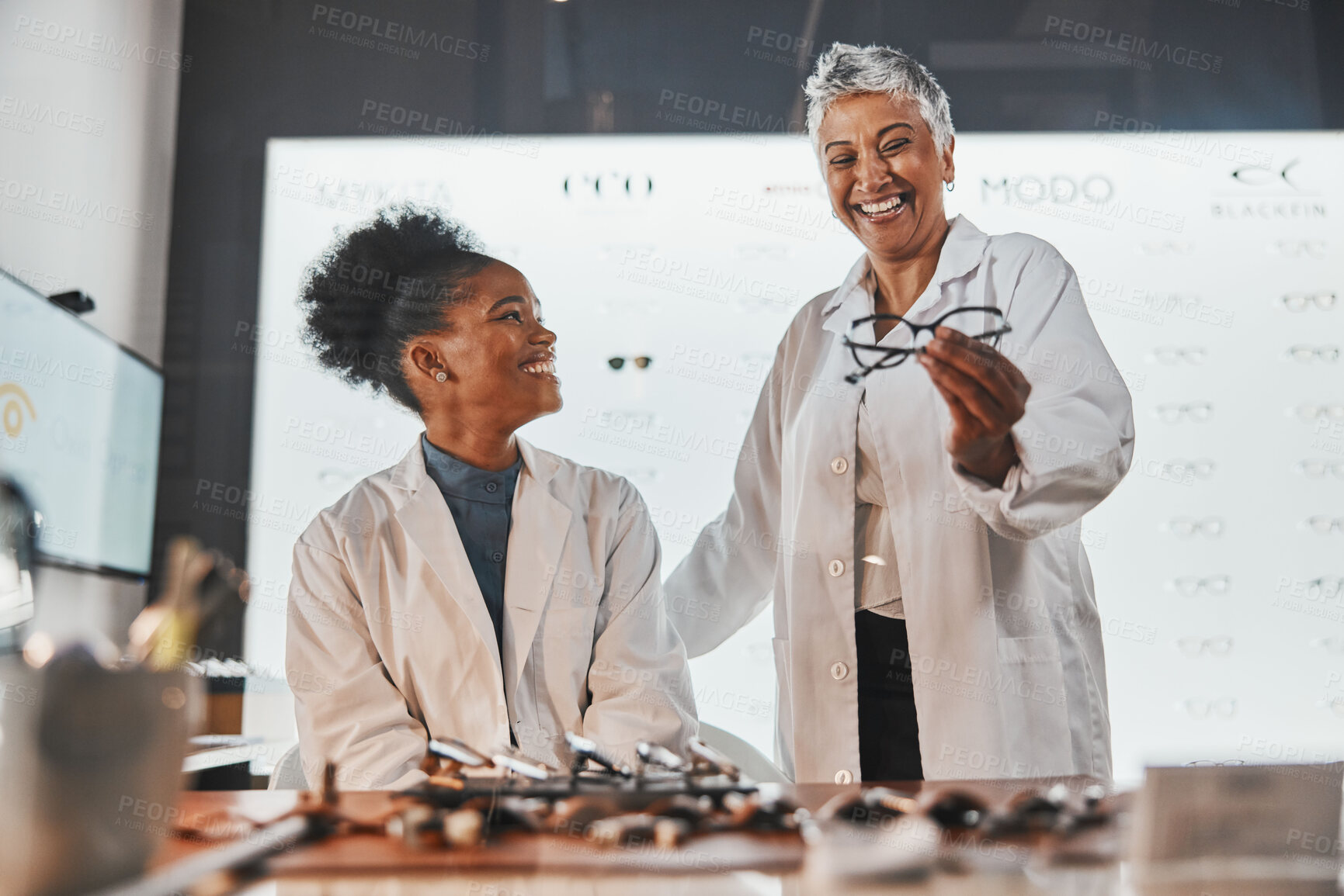 Buy stock photo Glasses, optometrist teamwork and women in shop or store for frames, eyewear or eye care spectacles. Ophthalmology, vision and happy senior optician laughing at funny joke or comedy with black woman.