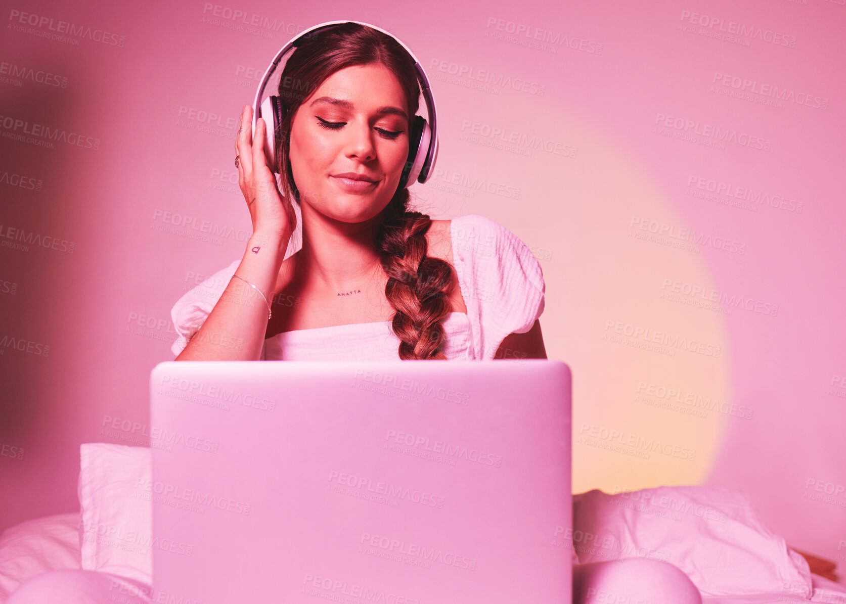 Buy stock photo Pink, light and laptop by woman in a bed with music, social media and streaming on wall background. Podcast, website and girl relax in bedroom, happy and enjoying radio, audio or online playlist