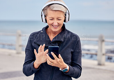 Buy stock photo Senior woman, phone and headphones listening to music by the beach with smile for audio track. Happy elderly female smiling with smartphone for online streaming or 5G connection by the ocean coast