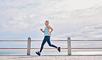 Senior woman running outdoor at on sky mockup at beach promenade for energy, health and cardio workout. Elderly female, exercise and runner at ocean for sports training, fitness and healthy marathon