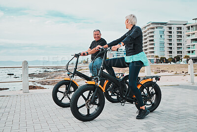 Mature couple, electrical and bike by ocean, beach or sea in bonding transportation, clean energy or sustainability travel. Ebike, electricity and eco friendly bicycle for happy man or cycling woman