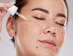 Face, eyes closed and skincare of woman with serum in studio isolated on a gray background. Dermatology skin, beauty cosmetics and female model apply hyaluronic acid, essential oil or retinol product