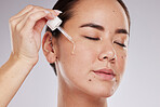 Eyes closed, face and skincare of woman with serum in studio isolated on a gray background. Dermatology skin, beauty cosmetics and female model apply hyaluronic acid, essential oil or retinol product