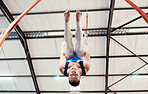 Man, acrobat and gymnastics upside down on rings in fitness for practice, training or workout at gym. Professional male gymnast hanging on ring circles for athletics, acrobatics or strength exercise