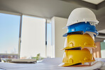 Building, helmets and architect equipment on table for construction safety, security or industrial work gear at office. Stack of hard hats on desk for safe engineering or contracting for architecture