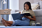 Student, writing and black woman with book in home living room for learning, studying and knowledge. Laptop, education and smile of happy female with notebook for notes, information and research.