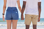 Interracial, couple and hands holding on the beach on vacation, holiday or trip together bonding at sea or ocean. Date, back view and closeup of people with love on a break on a weekend in nature