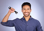 Portrait of man holding wrench isolated on studio background for repair solution, maintenance or plumbing. Professional worker, asian person or happy plumber with mechanic tools hand in job success