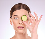 Woman, face and hand with cucumber for skincare nutrition or healthy diet against a gray studio background. Portrait of female holding vegetable for organic facial treatment or natural cosmetics