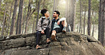 Nature, hiking and a couple relax on adventure trail in forest and sitting on a rock. Health, happy man and woman pointing at natural landscape while relaxing in woods with trees, fitness and freedom