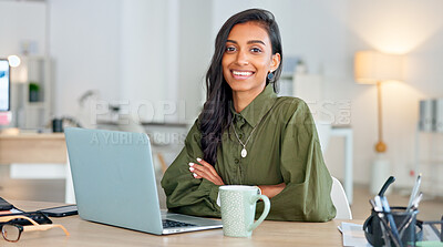 Proud, happy and confident business woman typing on a laptop and turns to look at the camera in her office. Portrait of a young female entrepreneur writing a project smiling in her workplace