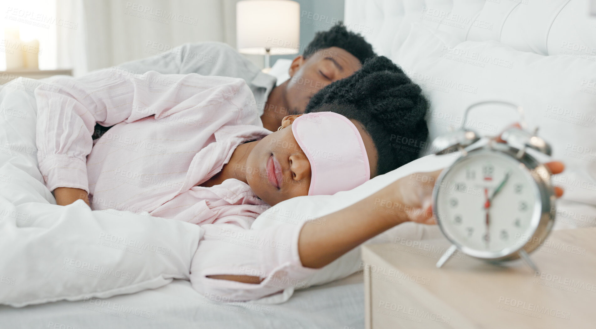 Buy stock photo Woman, sleeping and snooze alarm in bed with fatigue, tired or lazy in morning with man in home. Black couple, girl stop clock and rest in bedroom, house or annoyed in mask at wake up time with dream