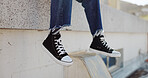 Rooftop, shoes and man in an urban city sitting on the top of a building for a view of the cityscape. Hipster, freedom and closeup of male feet with sneakers hanging from an outdoor roof in town.