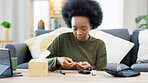 Happy African American woman using a glucose monitoring device at home. Smiling black female checking her sugar level with a rapid test result kit, daily routine of diabetic care in a living room