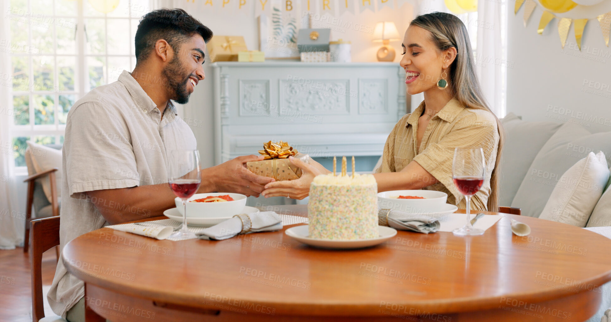 Buy stock photo Birthday cake, giving gift and food with couple, love and date in home living room with drink. Happy, smile and people at table with conversation and celebration dessert with alcohol and talking