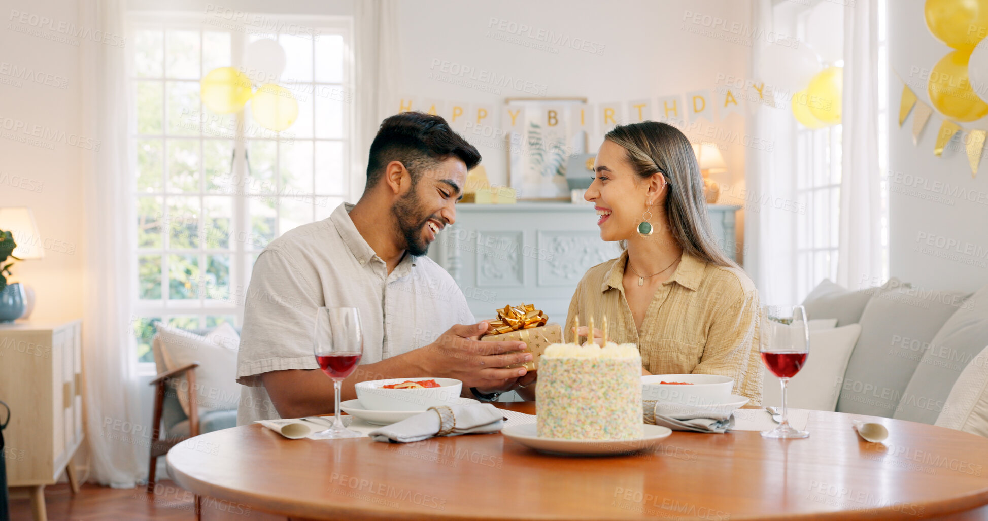 Buy stock photo Birthday cake, celebration and gift with interracial couple, love and date in home living room with drink. Happy, smile and people at table with conversation and dessert with alcohol and talking