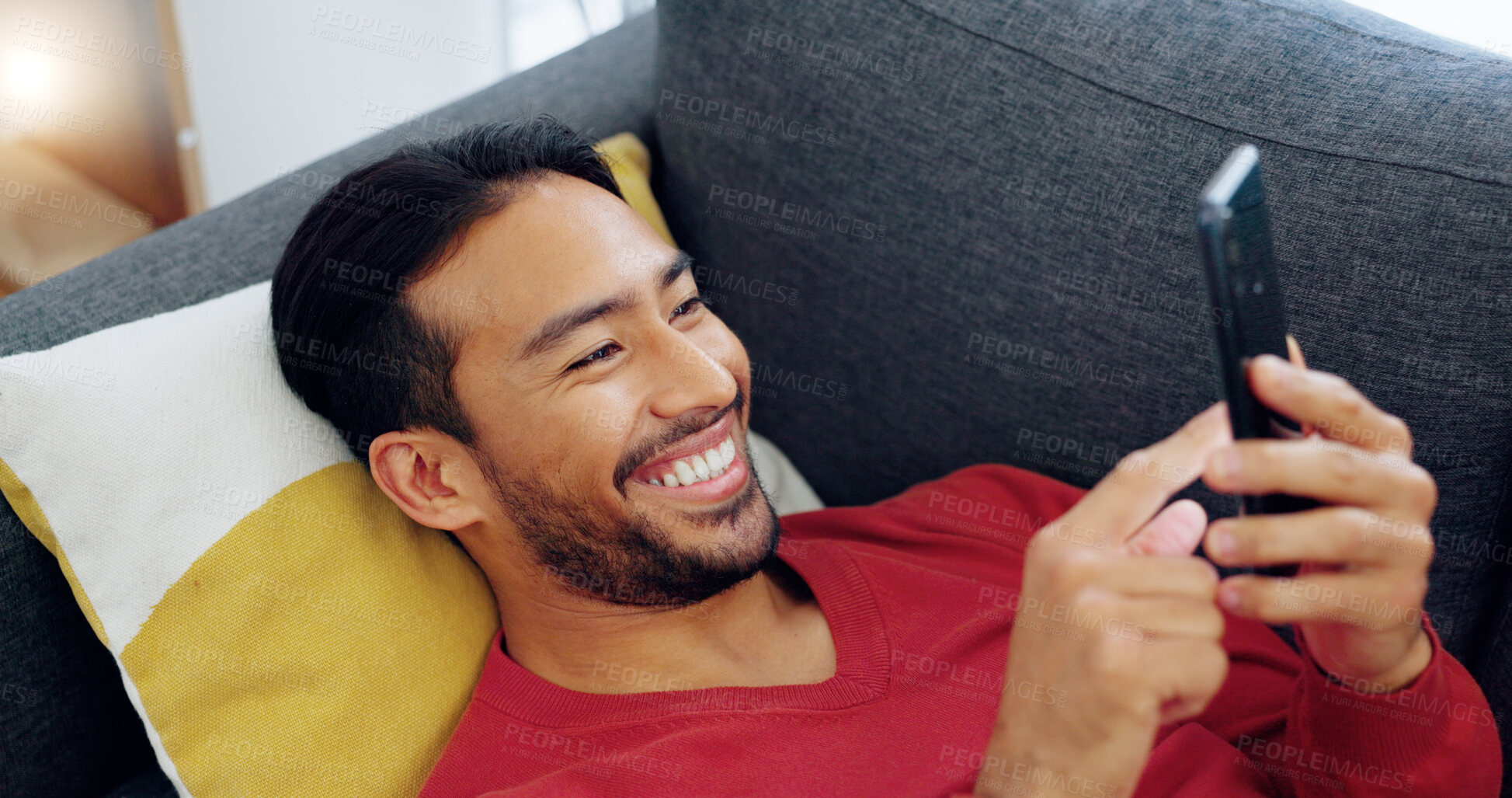 Buy stock photo Phone, laugh and Asian man on sofa with social media, comic or smile at funny text while streaming at home. Happy, smartphone and Japanese male in a living room with app, meme or gif communication