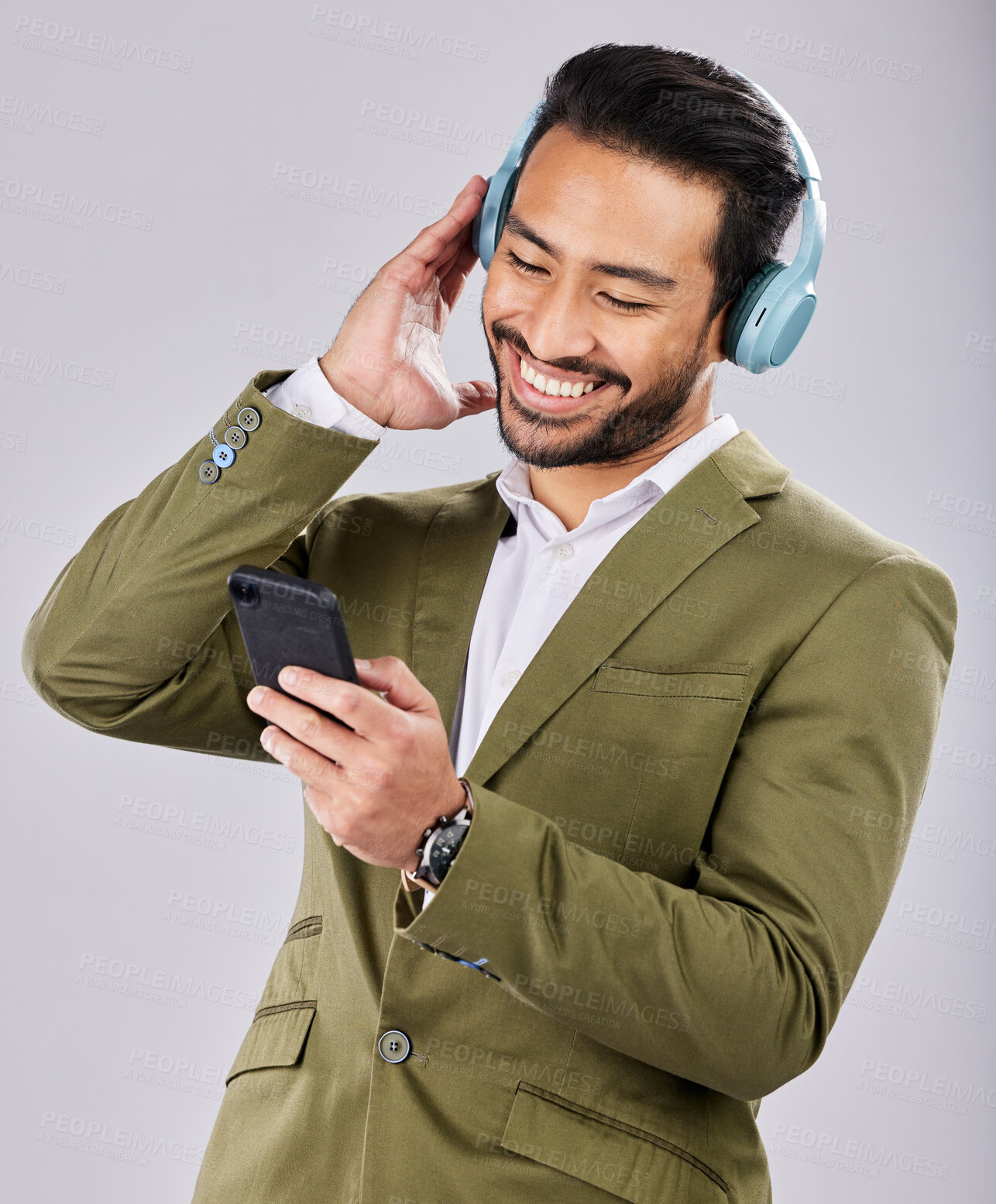 Buy stock photo Asian man, phone and smile listening to music on headphones against a gray studio background. Happy formal male smiling on smartphone with headset for audio streaming or entertainment on mobile app