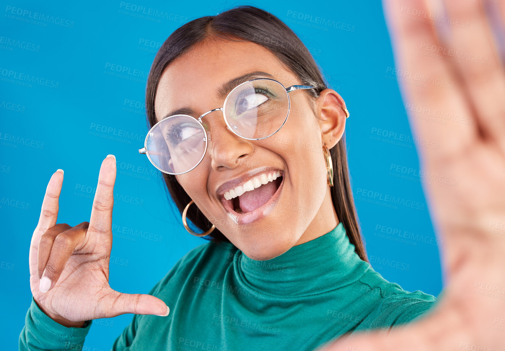 Buy stock photo Woman, face and fashion selfie with rock on hand for gen z attitude on a blue background with glasses. Happy model person in studio with excited and cool hand sign or emoji with beauty and motivation