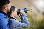 Binoculars, pointing and a couple bird watching in nature while hiking in the mountains together. Forest, nature or sightseeing with a man and woman looking at the view while bonding on a hike