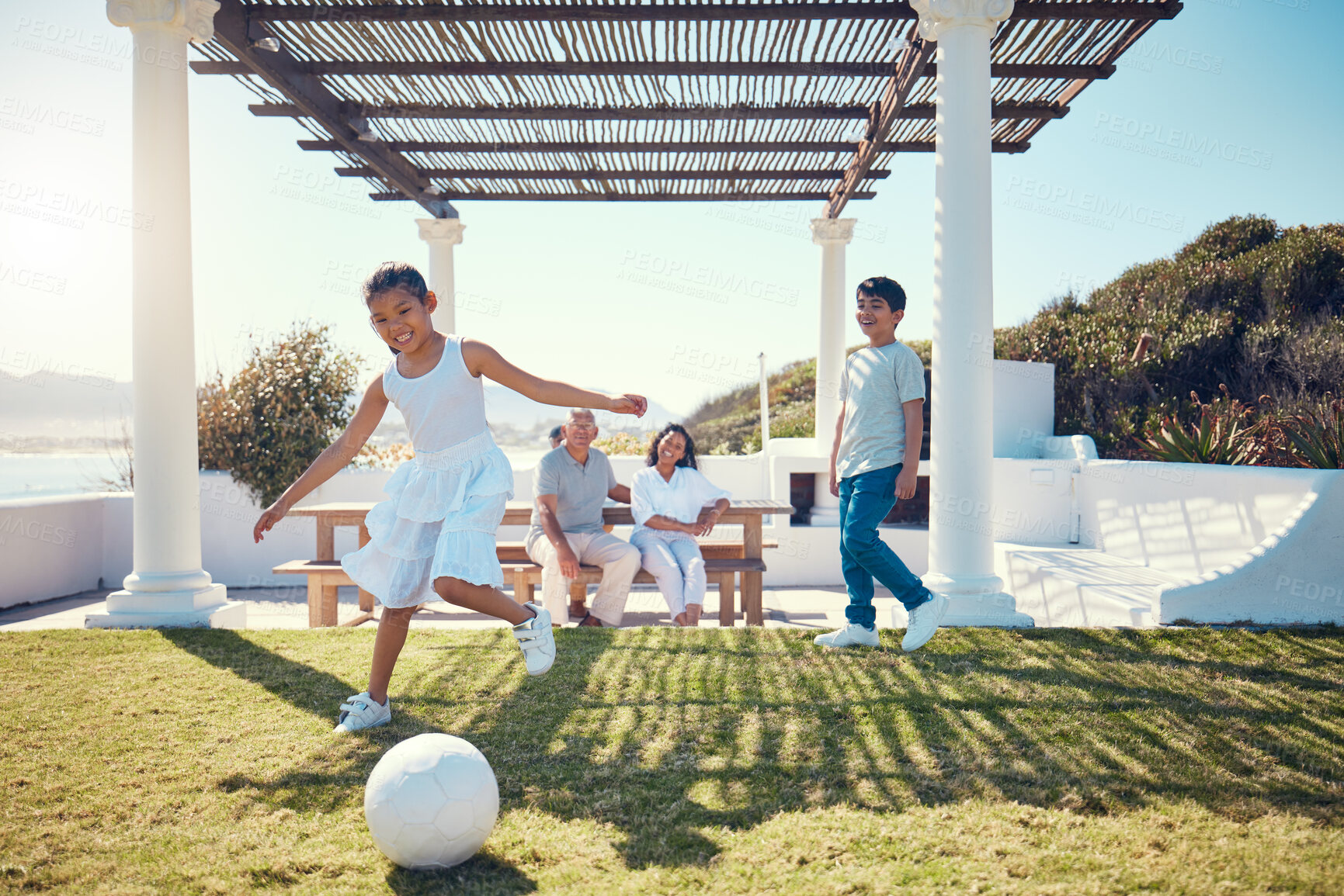 Buy stock photo Family, vacation and children playing soccer on a lawn in a holiday house and girl kick a ball having fun outdoors. Happy, excited and grandparents watch kids on the grass to play football 