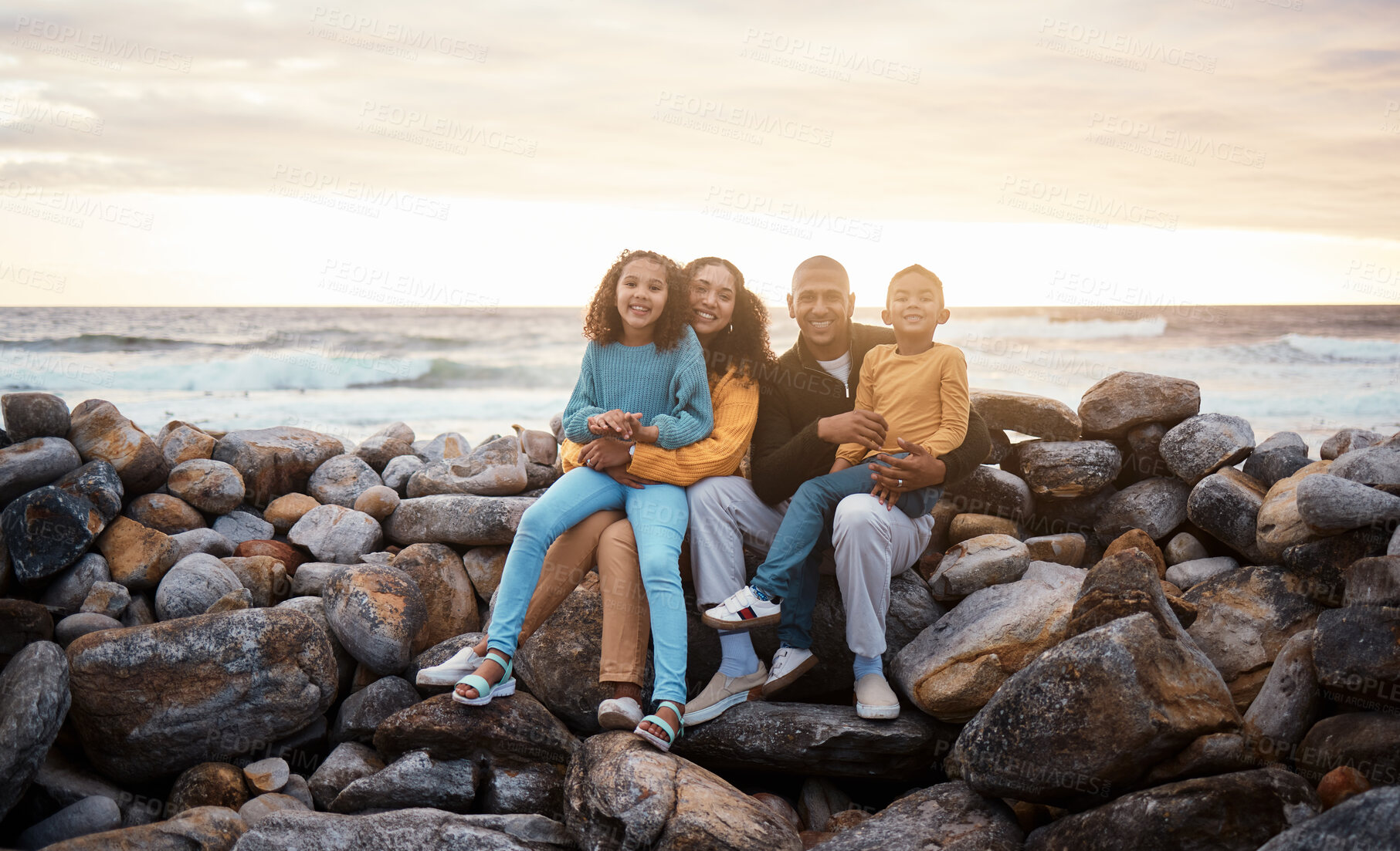 Buy stock photo Black family, parents and children in beach portrait with excited face, sitting and rocks with happiness. Black woman, man and kids by ocean with love hug, care and bonding on holiday by sunset sky