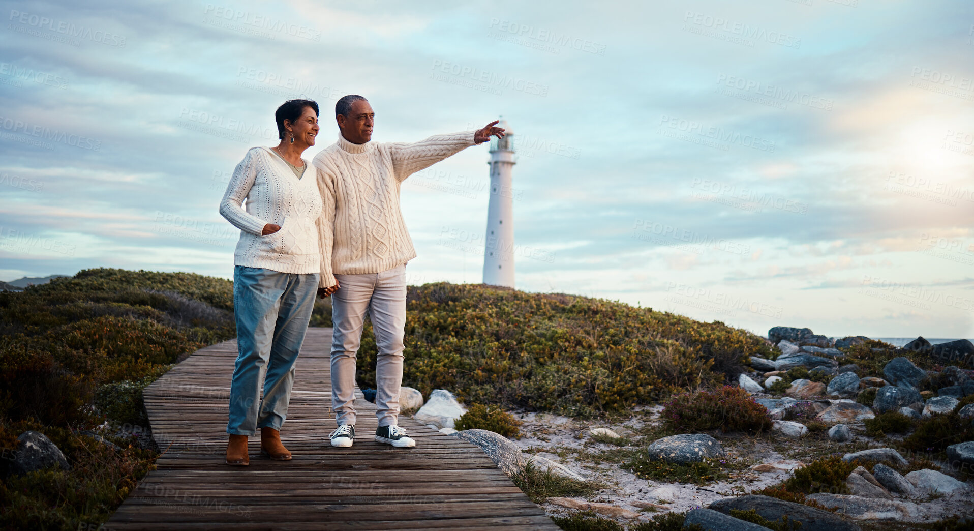 Buy stock photo Travel, love and elderly couple pointing on boardwalk at beach, calm at a lighthouse against sunset sky. Senior, man with woman on ocean trip, holiday or vacation, happy and enjoying retirement