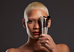 Woman, portrait and makeup brushes for facial beauty cosmetics, skincare or treatment against a gray studio background. Beautiful female holding cosmetic brushing tools on face for self care or love