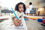 Child hand, coloring homework and pencil art of a girl lying on a living room carpet at home. House, color learning and creative development activity of young kid in kindergarten with  a school book