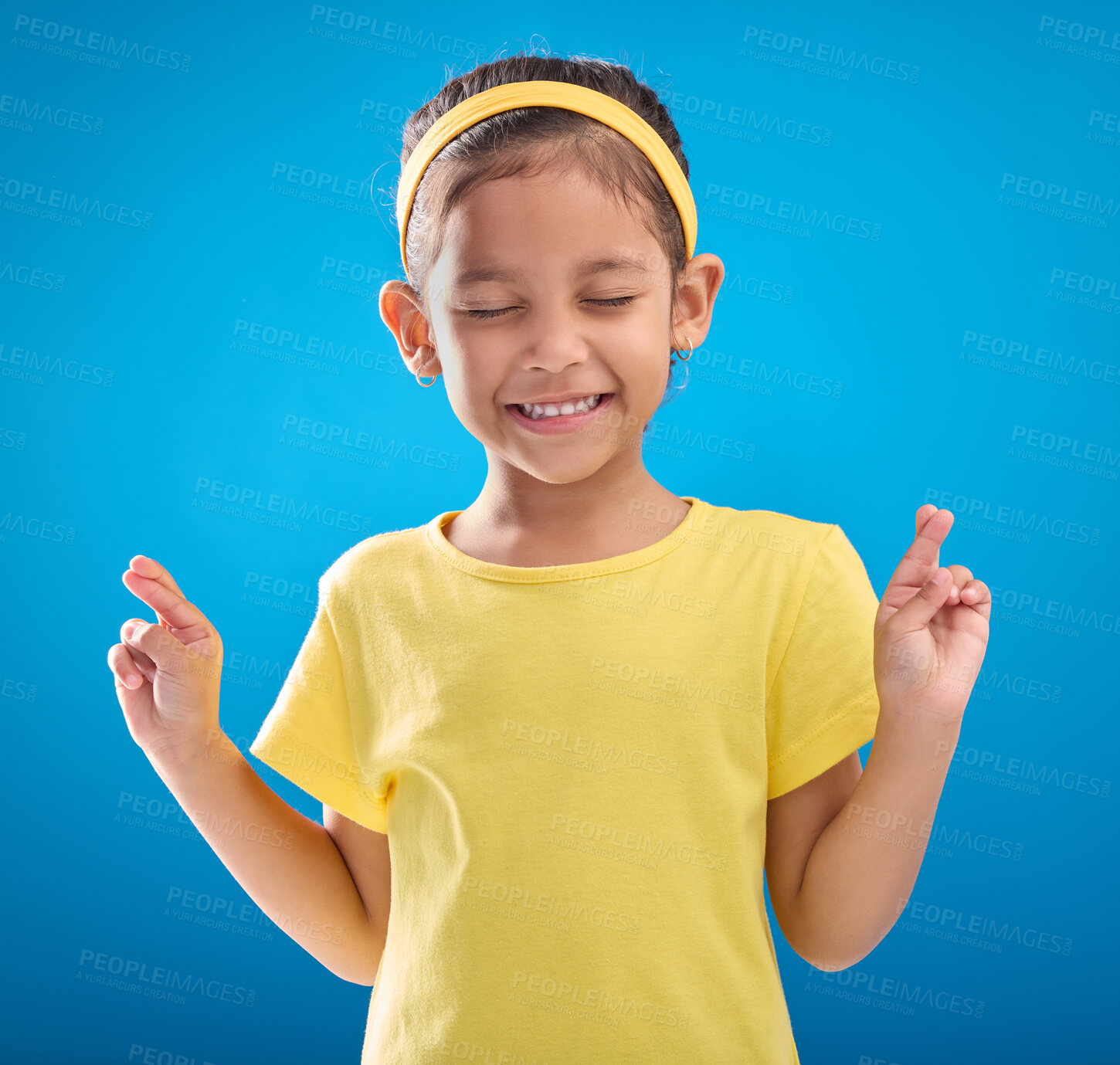 Buy stock photo Child, hand and fingers crossed in studio for hope, wish or good luck against a blue background. Girl, eyes closed and emoji hands, praying and wishing, happy and smile while posing on isolated space