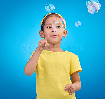 Buy stock photo Children, cute and a girl popping bubbles on a blue background in studio for fun or child development. Kids, motor skills and pointing with a female youth playing a game alone on a color wall