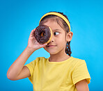 Donut, eye and cover of girl in studio for junk food, sugar and happiness. Snack, cake and cute with face of young child and dessert for cute, positive and chocolate isolated on blue background