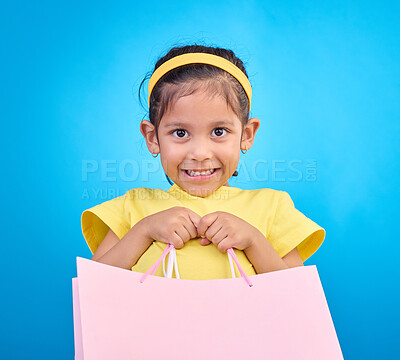 Buy stock photo Girl smile, portrait and gift bags from birthday party, event or celebration with a present in studio. Shop choice, bag and little child looking at presents with isolated and blue background with kid