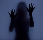 Shadow, glass and hands with a woman in studio on a blue background for mystery or sensual secrecy. Creative, silhouette and window with a female posing for beauty, art deco or feminine desire