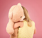 Teddy bear, love and back of a girl in a studio with a big, fluffy and cute toy as a gift or present. Adorable, innocent and young child hugging her teddy with care and happiness by a pink background