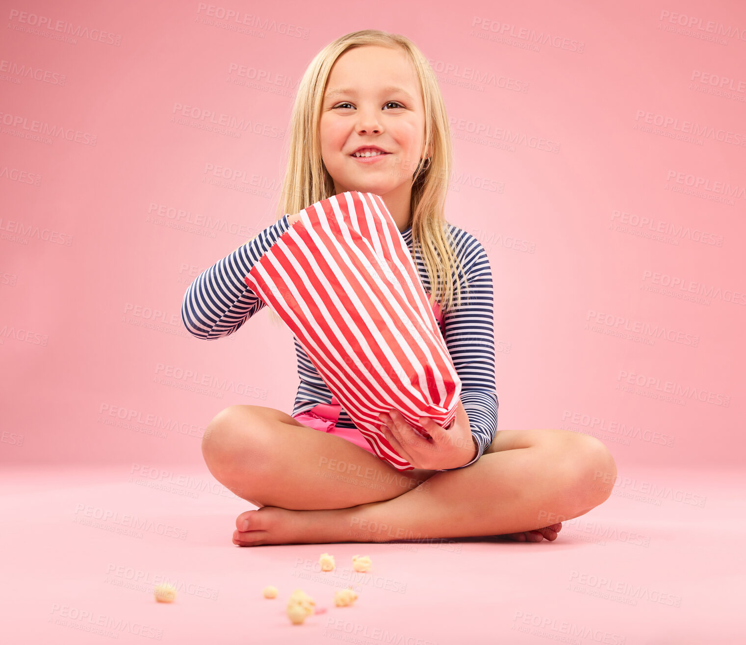 Buy stock photo Popcorn, snack and happy girl in a studio with pink background sitting with movie snacks. Food, happiness and hungry young child with a paper bag and chips eating and feeling relax with a smile